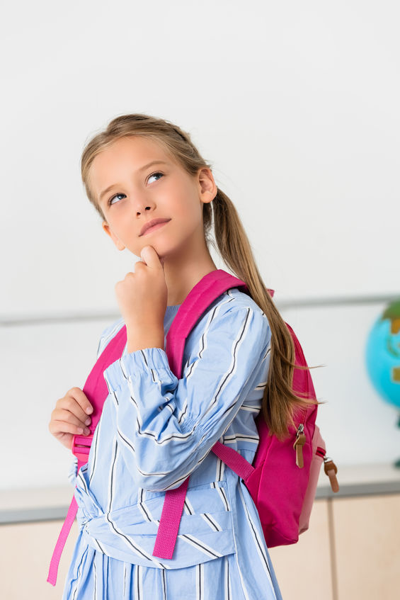 Dreamy schoolgirl with backpack looking away in classroom